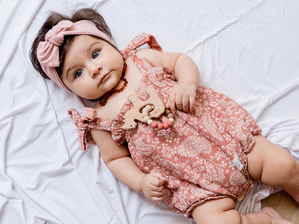 Baby wearing a terracotta patterned romper and a pink bow headband.